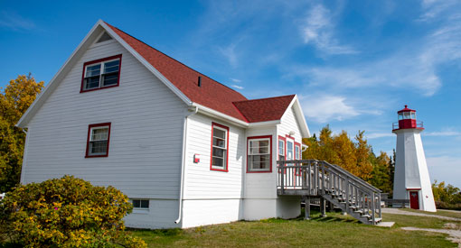 Une maison blanche au toit rouge avec un phare en arrière plan. 