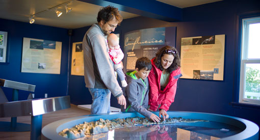 A woman, a man, a child and a baby visit an exhibition and look at a model. 