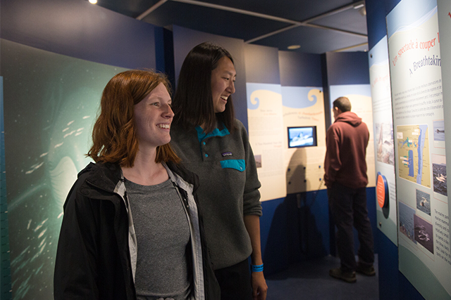 Two young women read an information panel in an indoor exhibition. 
