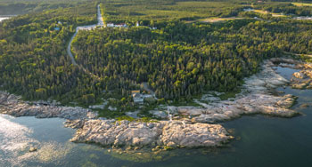Le Cap-de-Bon-Désir vu depuis la rive du Saint-Laurent. En arrière plan, un chemin d'accès au coeur de la forêt permet de se rendre à l'ancienne station de phare. Un sentier se poursuit jusqu'aux rochers en bordure du Saint-Laurent. 