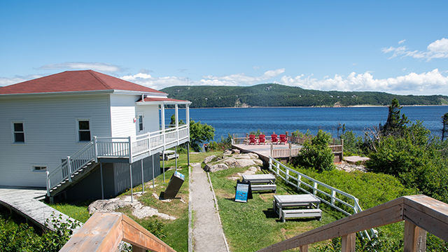 A white house with a red roof on the left and observation points with picnic tables and red chairs on the right.