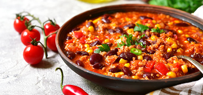 Un bol de chili et de tomates cerises est posé sur une nappe blanche.