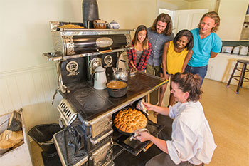 A group of visitors watch an interpreter take a hot pie out of a stove