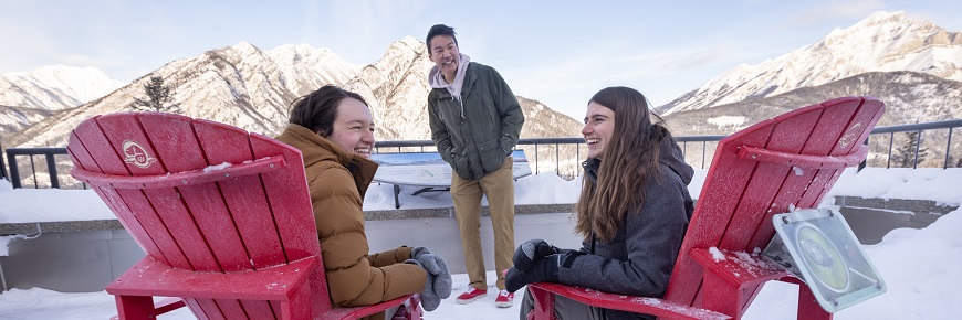 three people sat on red chairs chatting with snowy mountains in the background