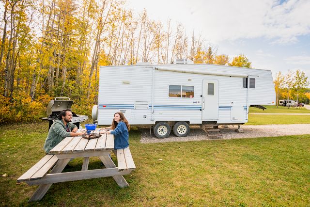 Deux visiteurs s'assoient à une table de pique-nique devant leur véhicule récréatif dans une aire de camping-car