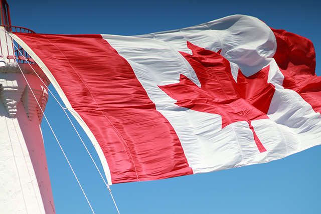 A giant Canada flag hanging from the top of the Fisgard lighthouse tower flying in the wind.