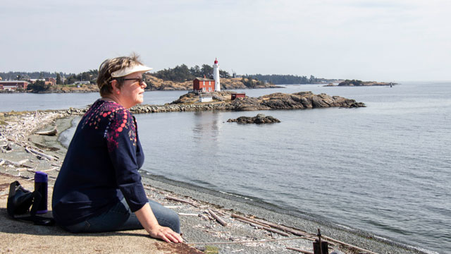 Assise, une retraitée se relaxe en observant la view du détroit de Juan de Fuca. Le phare de Fisgard est en arrière-plan