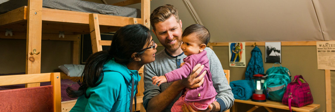  Inside an oTENTik, two parents play with their baby. The oTENTik bunkbeds are visible behind them. 