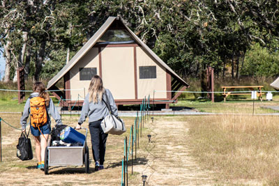 A couple travels towards the oTENTiks with a wheelbarrow carrying their gear.