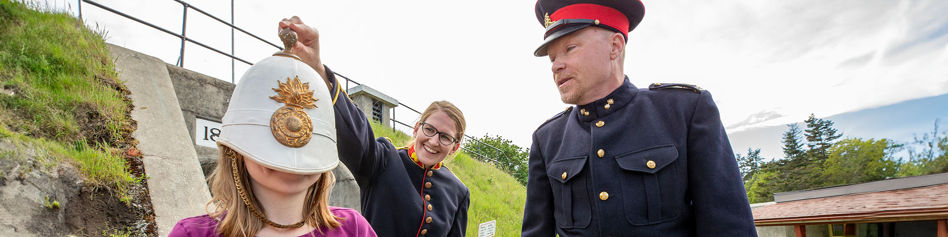 Une petite fille essaye un casque de la Royal Navy avec l’aide de guides-interprètes en uniforme d’époque.