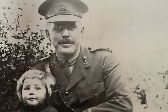 An officer in uniform and his son are sitting on a rock in the 1930s.