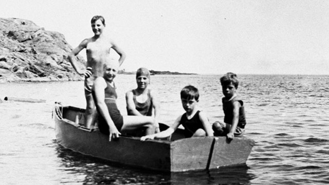 A group of children in a wooden boat on the water, circa 1920s.