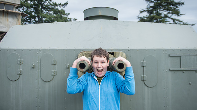 a young person poses for a photo in front of a large canon.