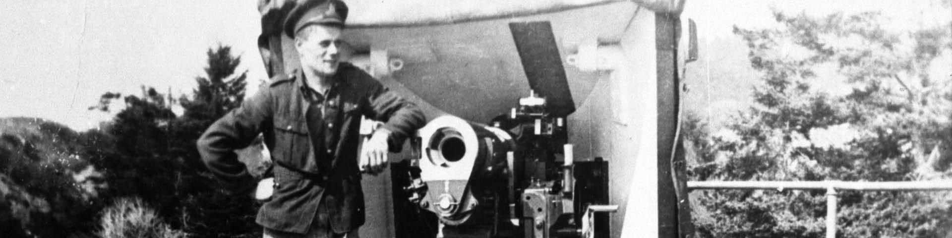 Photo historique en noir et blanc d'un soldat posant à côté d'un canon antiaérien, portant un uniforme militaire.