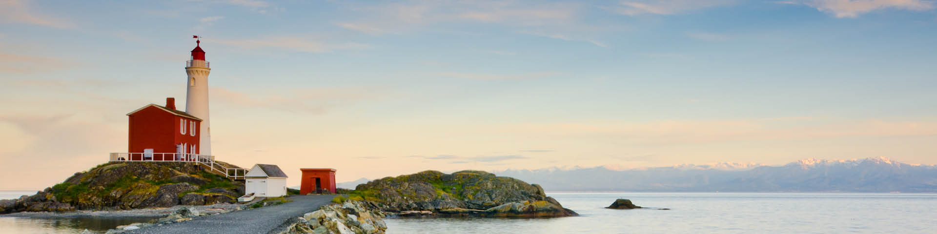 A lighthouse with a mountain range in the background, bathed in the warm light of the golden hour.