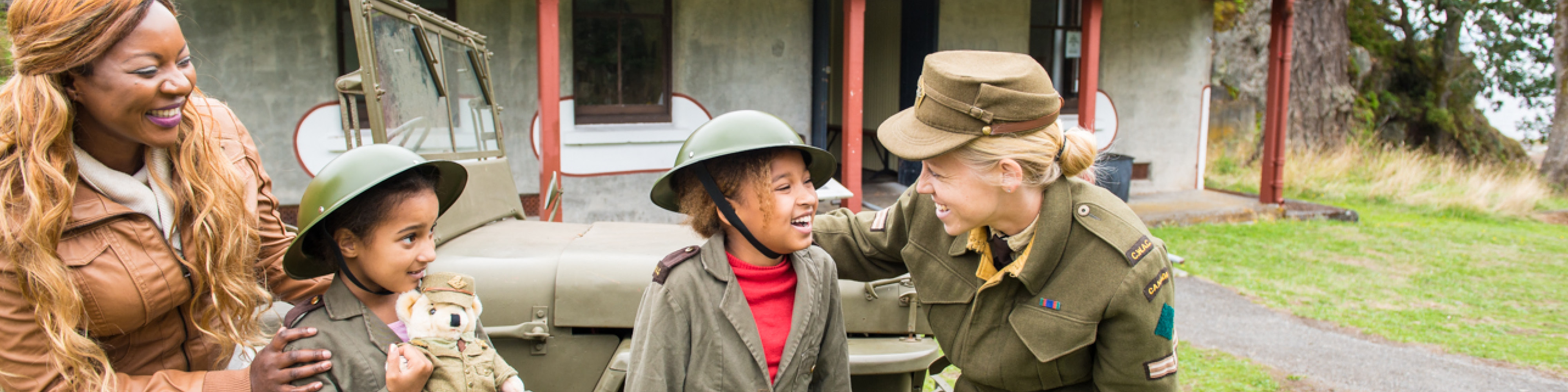 A staff member helps two students try on historical military hats. 