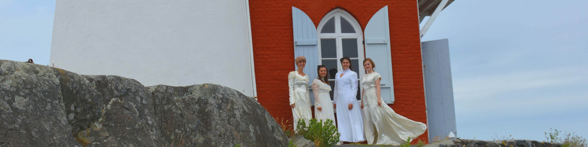 Four interpreters dressed in 1940s-style wedding dresses pose in front of a lighthouse building.