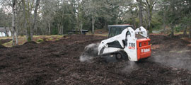 A mechanical Bobcat spreads mulch evenly on the ground.