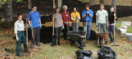 A group of volunteers stand with shovels in their hands and wheelbarrows nearby.