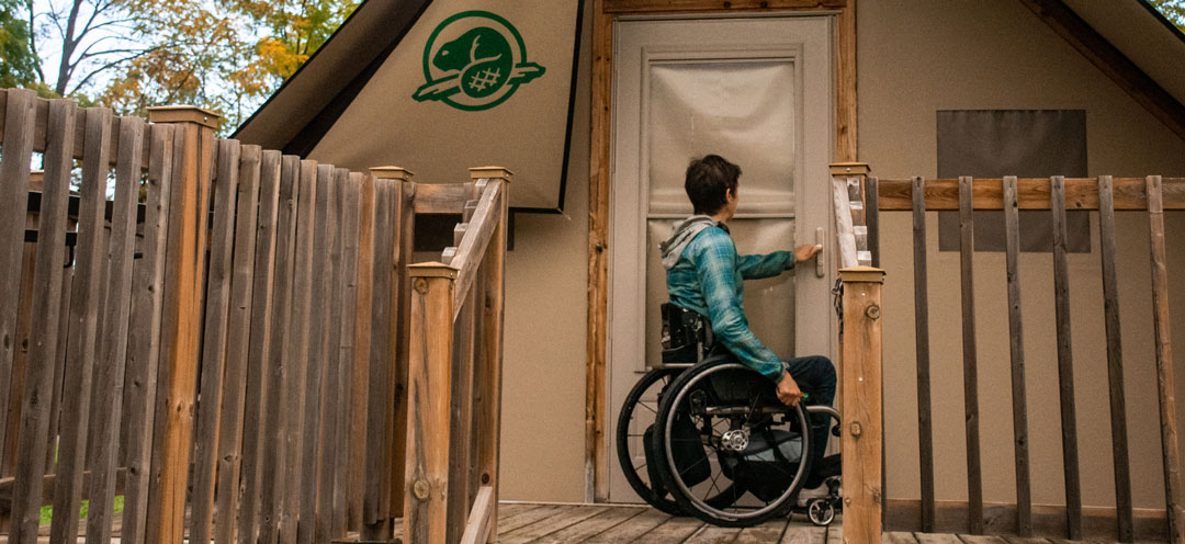 A person in a wheelchair opens the door to an oTENTik cabin.