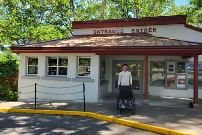 A Parks Canada staff member in uniform stands at the historic site’s main entrance with a wheelchair ready to use.