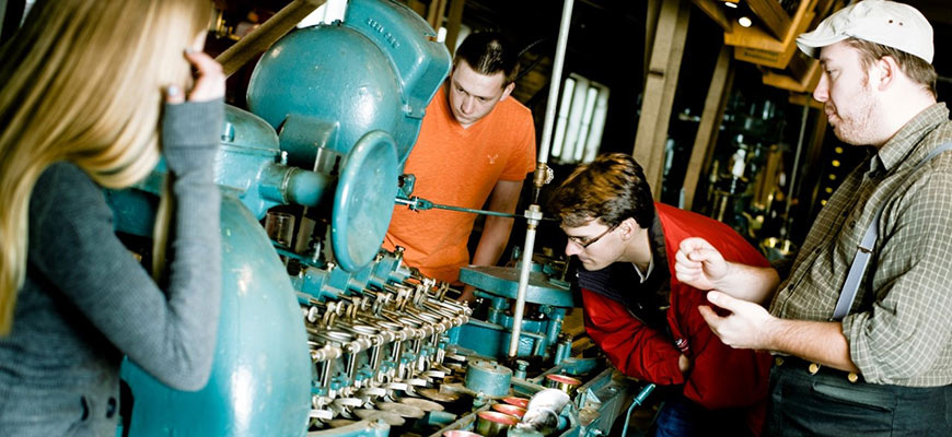 A group of adults interact with a large historical machine. 