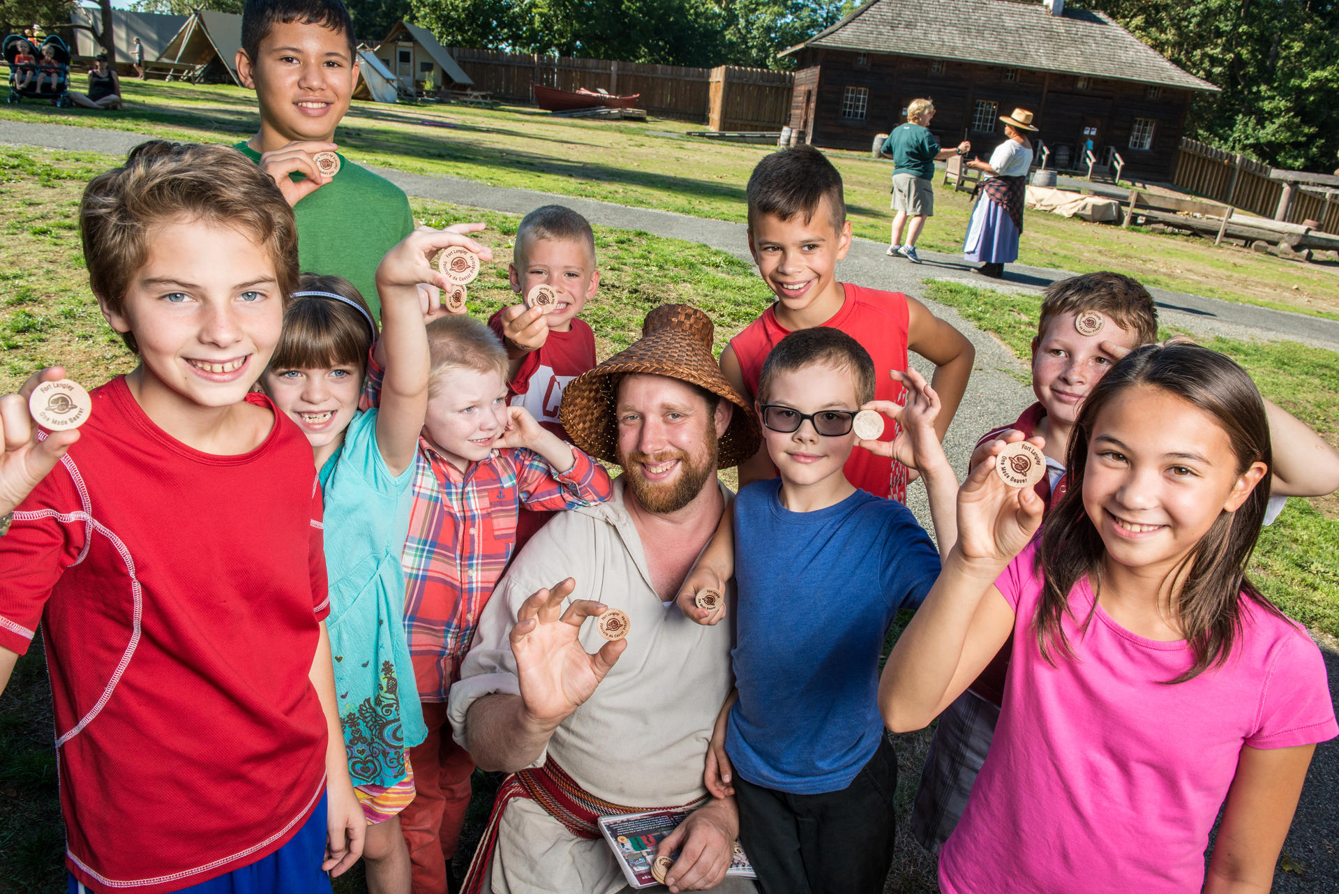 A costumed interpreter and a group of children show off their ‘beaver coin’ swag. Fort Langley National Historic Site. 