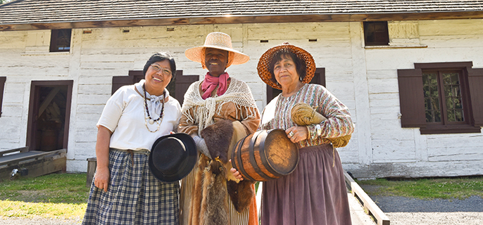 Three costumed interpreters in front of the Storehouse building.