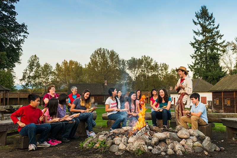 Group of people sitting around a fire at Fort Langley National Historic Site.