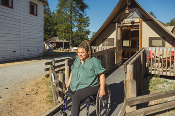 Un visiteur séjournant dans une tente oTENTik accessible descend la rampe en fauteuil roulant.