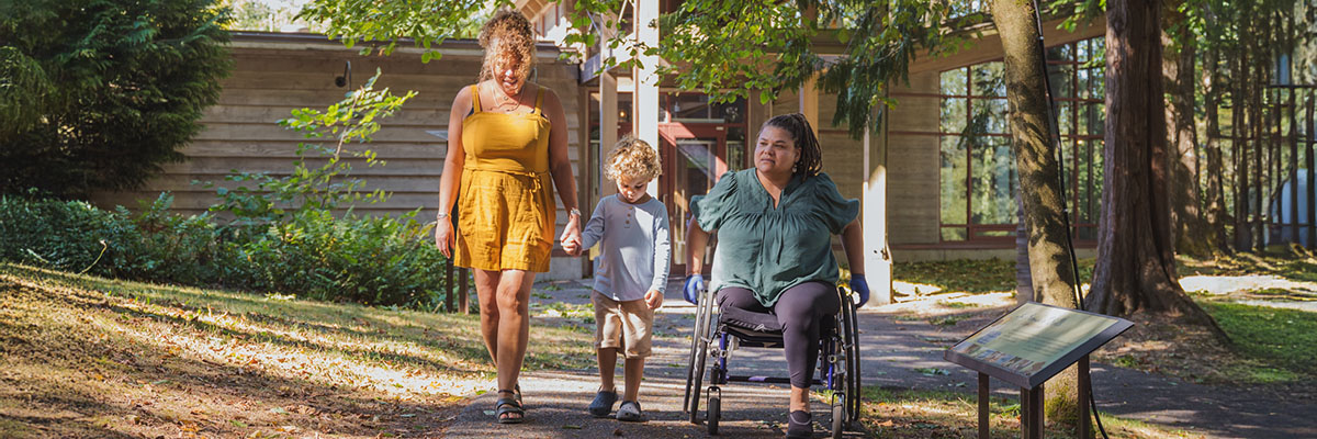 Quelques personnes se dirigent vers le Centre d’accueil depuis le stationnement. L’une d’elles utilise un fauteuil roulant manuel