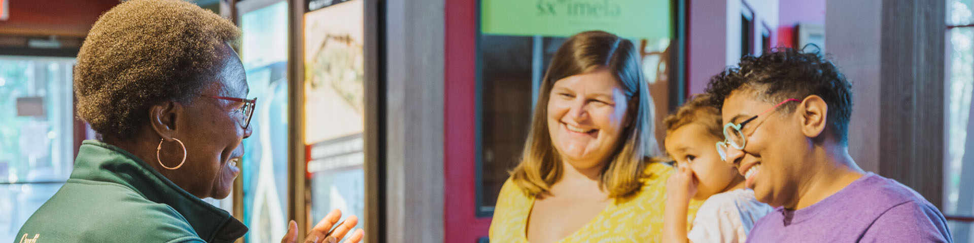 A parks employee talking to two individuals and their child from behind a counter while the three individuals smile at each other.