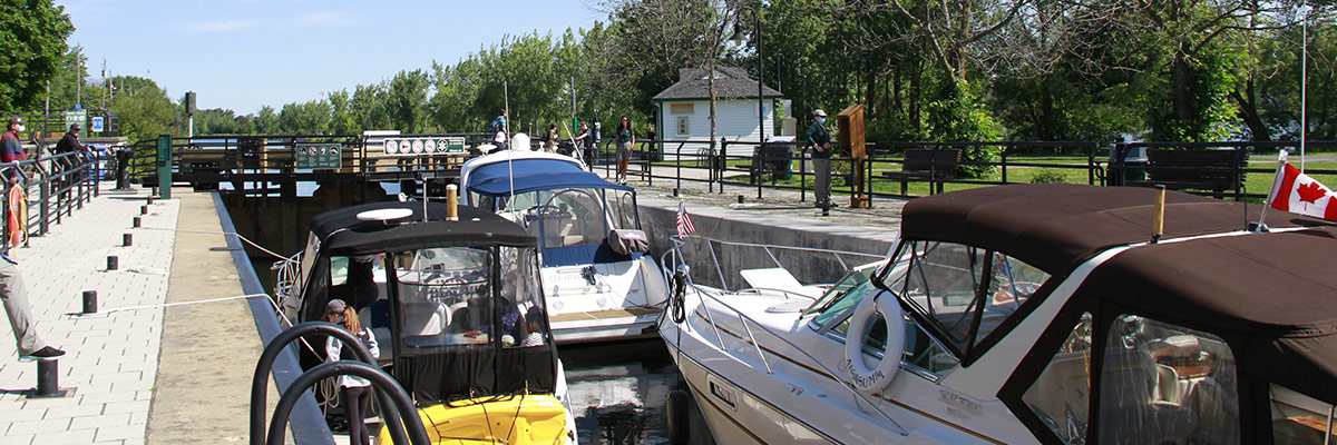 Bateaux de plaisance dans une écluse d’un canal historique pendant une manœuvre d’éclusage, avec des visiteurs et des employés sur le quai.