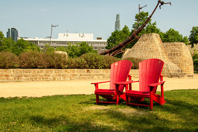 Two red Adirondack chairs in front of a gravel path and a brick cultural installation.