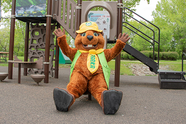 Une mascotte de castor est assise au bout d’une glissade, les mains en l’air.