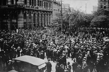 Photo en noir et blanc d’une importante foule de personnes rassemblées dans une rue en face d’un grand bâtiment.