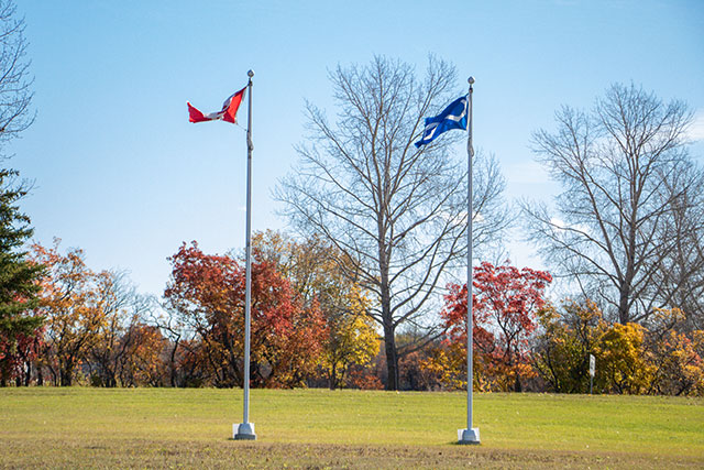 The Canadian flag and the Métis flag (blue with an infinity sign) blow in the wind.