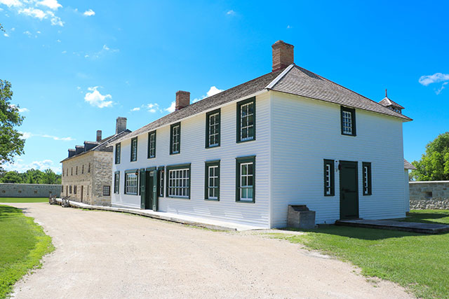 A gravel path leads to a wooden boardwalk and two-story white building.