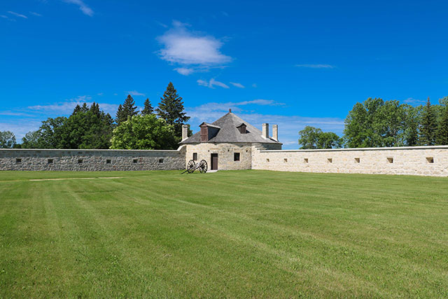 A stone bastion with a Red River cart sitting in the grass in front of it.