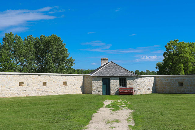 A stone bastion with a bench in the grass in front of it.