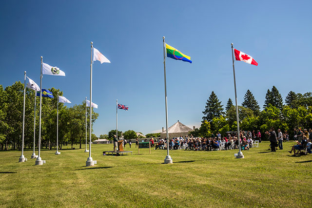 Nine flag poles in a C shape are shown with a flag raised to the top.