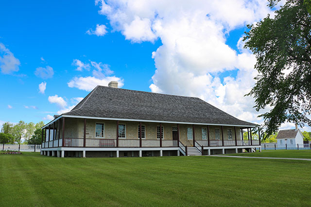 A stately home with wrap-around deck and a garden to the left of the image.