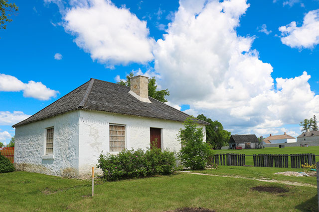 A small white house with some bushes in front of it and a wooden fence to the right.