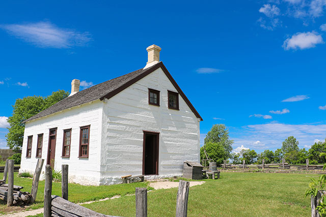 A small white house with a yard enclosed by a wooden fence.