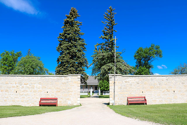 Un chemin de gravier menant à une entrée dans les murs de pierre avec la grande maison en arrière-plan.