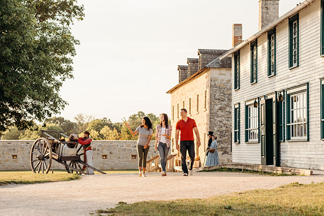 Three visitors walk on a gravel path at Lower Fort Garry National Historic Site.