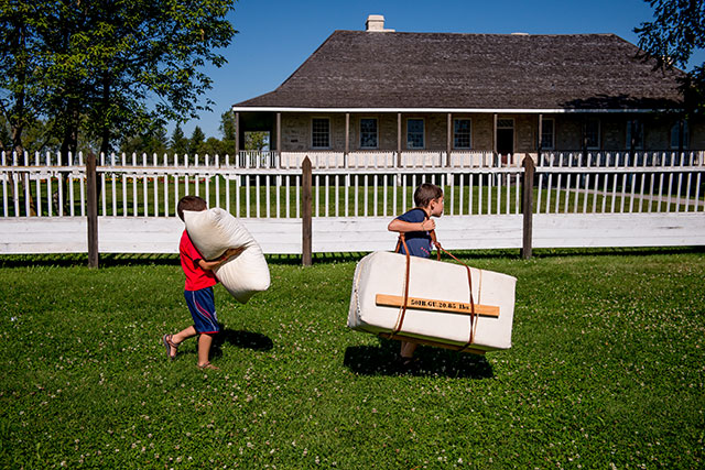 Two children visiting Lower Fort Garry carry replicas of fur trade bales as part of Children’s Day activities.