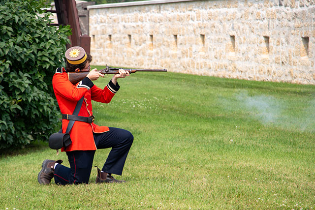 An interpreter in a North West Mounted Police uniform fires a blank from a rifle at Lower Fort Garry National Historic Site.