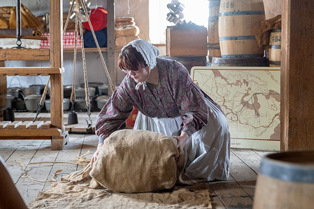 A Parks Canada employee in historic clothing kneels and secures a fur bale with cloth.