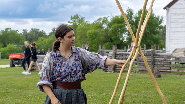 Une employée de Parcs Canada en tenue d’époque attache la base d’un mini tipi.